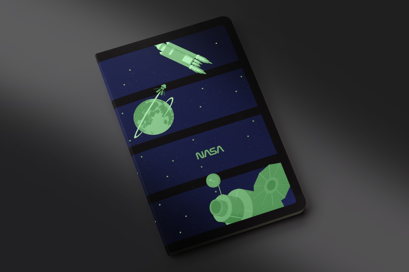 Softcover, Revista Volant Glow-in-the-Dark de la colección de cuadernos de edición limitada inspirada en la NASA por Moleskine. Hay cuatro paneles azul oscuro en una columna, cada uno con su propia imagen de escala de grises que brilla en la oscuridad. De arriba a abajo: cohete, tierra con satélite en órbita, texto de la NASA, satélite grande.