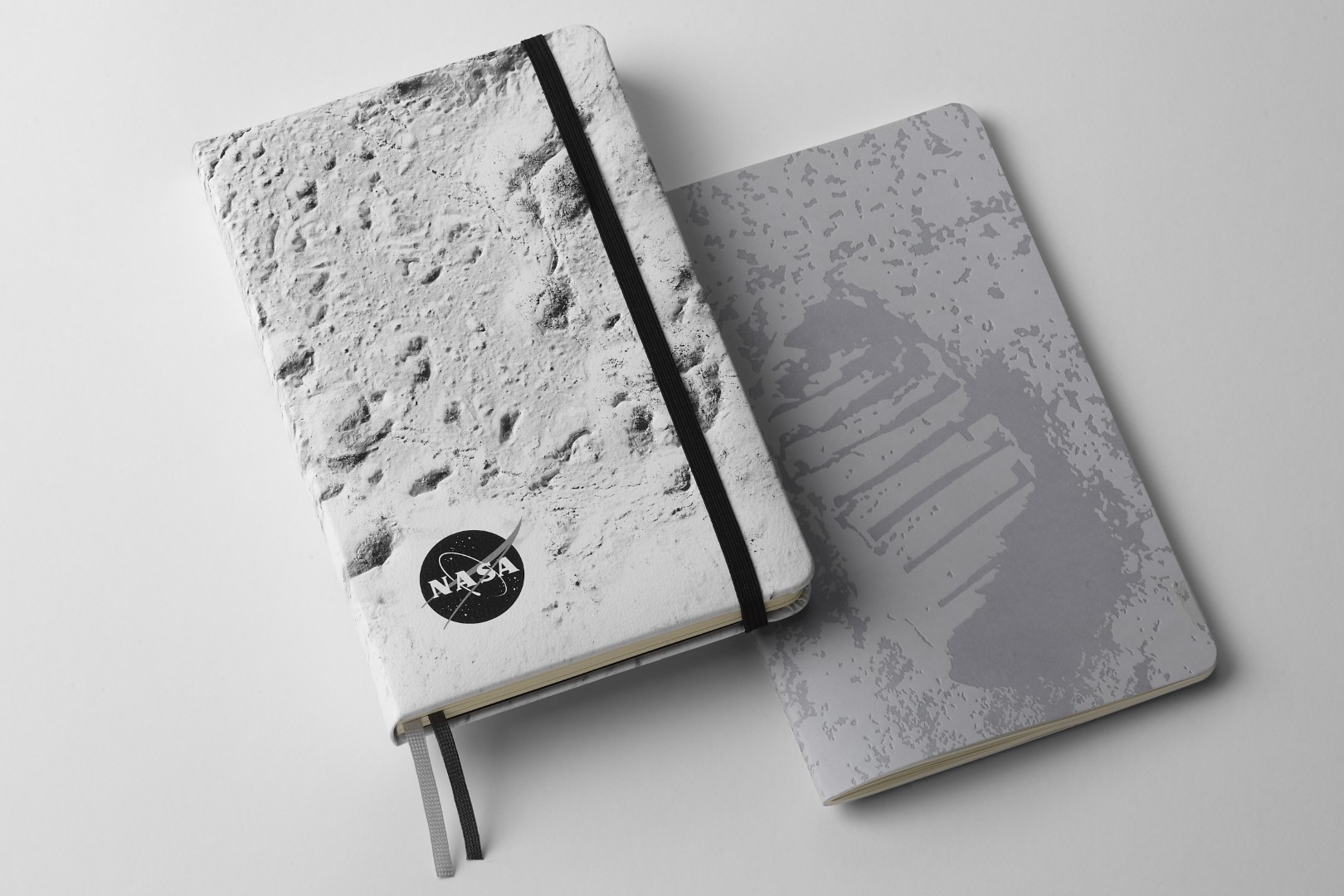 Notebook de edición limitada inspirada en la NASA de Moleskine. Izquierda: cuaderno con cubierta rígida con el primer piso de la luna en la portada de la luna. A la derecha: cobertura suave con la huella de Neil Armstrong en la luna en la portada.