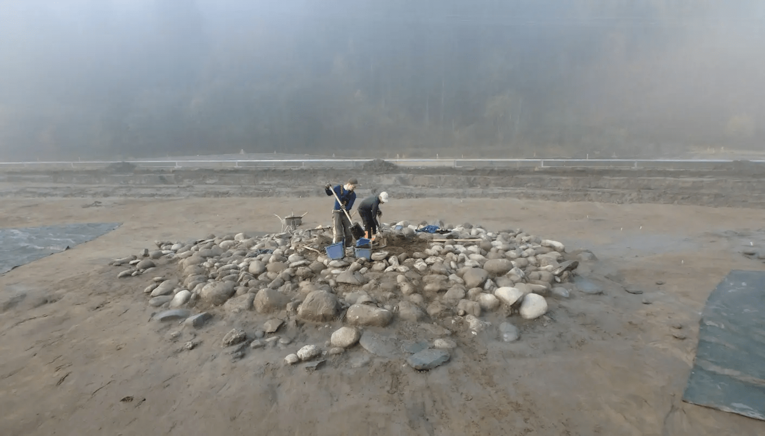 Dos arqueólogos que cavan entre las piedras para los montículos de entierro en el día brumoso