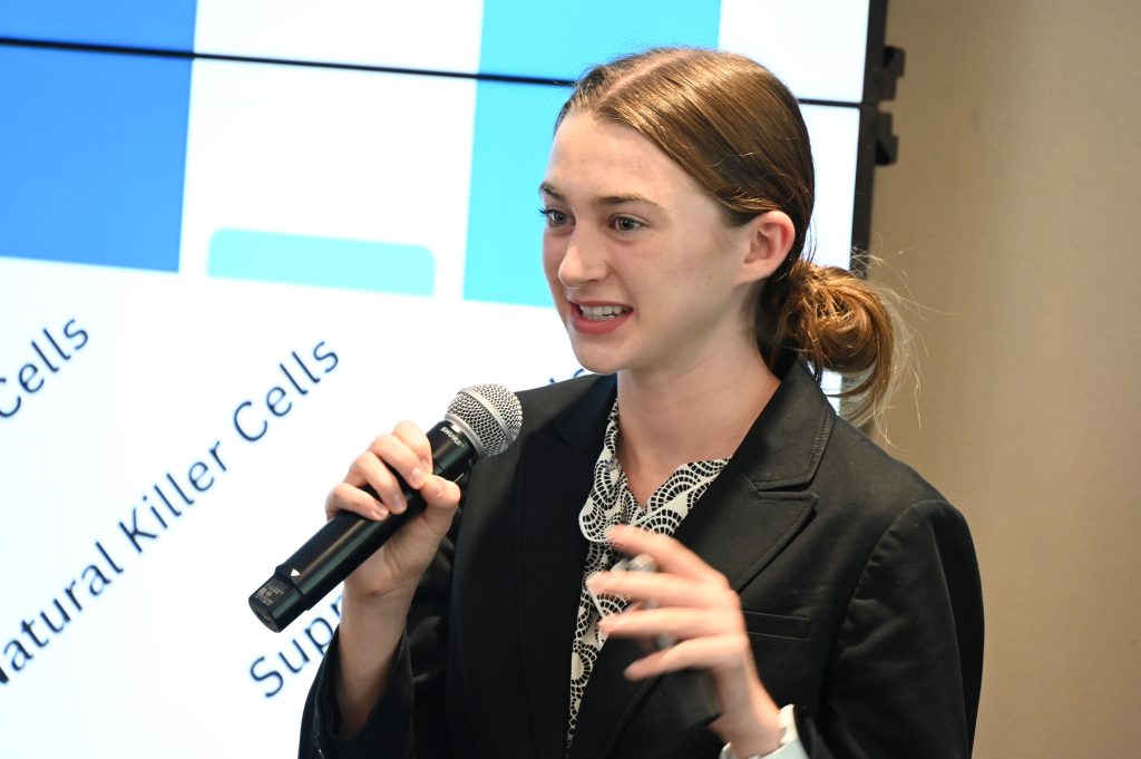 Un estudiante de secundaria presenta una presentación frente a un grupo grande. Describe su experiencia aprendiendo sobre la investigación en un laboratorio.