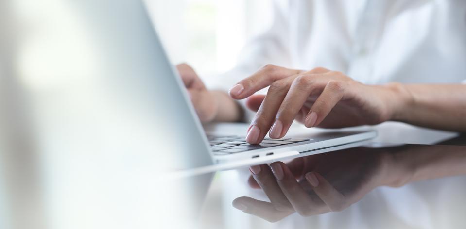 Primer plano de mujer de negocios escrito a mano en el teclado de la computadora portátil con reflexión sobre la tableta digital en la tabla de oficinas, trabajo en línea, navegar por Internet, trabajo distante, concepto de trabajo remoto