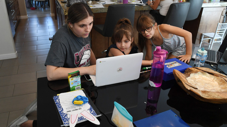 Un adolescente mirando un Chromebook junto a dos niños