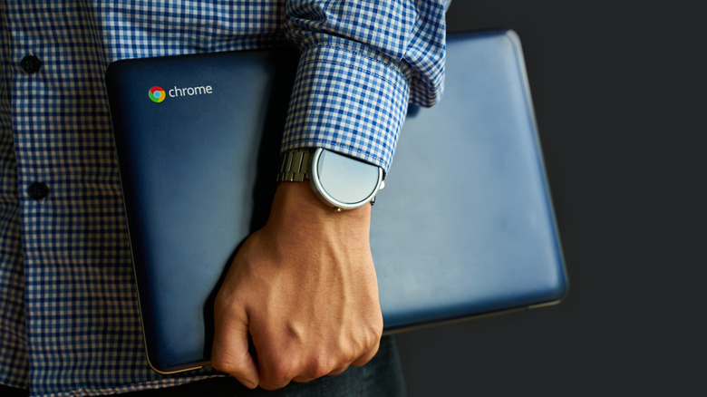 La mano de un hombre sosteniendo un Chromebook con una camisa a cuadros azul