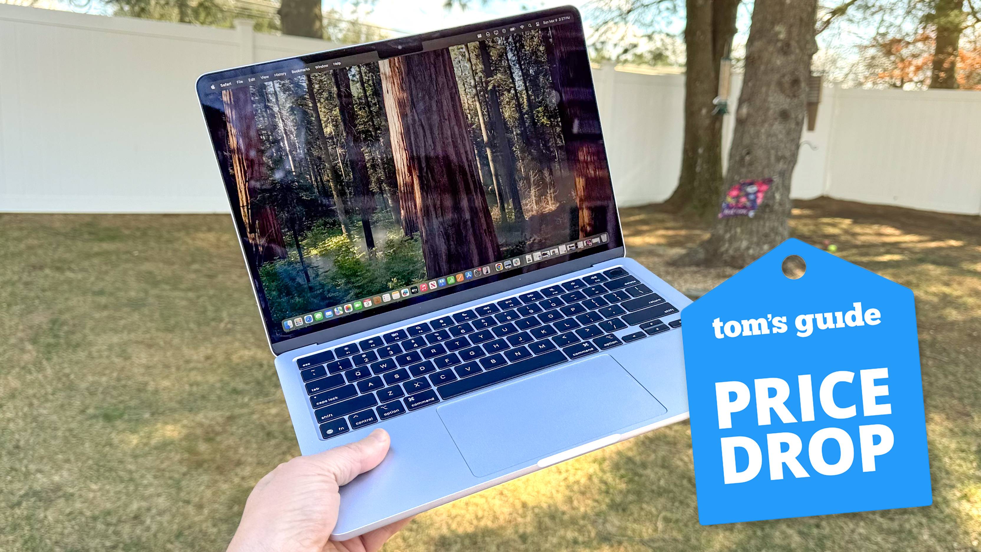 MacBook Air M4 en mano en el jardín con la insignia de caída de precio de Tom's Guide