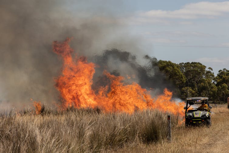 Un pequeño vehículo de extinción de incendios junto a un prado seco y en llamas.