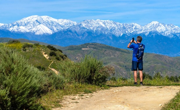 Un excursionista se detiene para tomar una fotografía de las montañas nevadas de San Gabriel mientras camina por el sendero Old Weir Canyon Trail en Anaheim Hills, el domingo 22 de febrero de 2026 por la tarde. (Foto de Mark Rightmire, para el Registro del Condado de Orange/SCNG)
