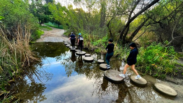 Los excursionistas usan escalones para cruzar Santiago Creek justo después del amanecer el sábado 28 de febrero de 2026, mientras se dirigen a los senderos para una caminata matutina en el Parque Regional Santiago Oaks en Orange. (Foto de Mark Rightmire, para el Registro del Condado de Orange/SCNG)