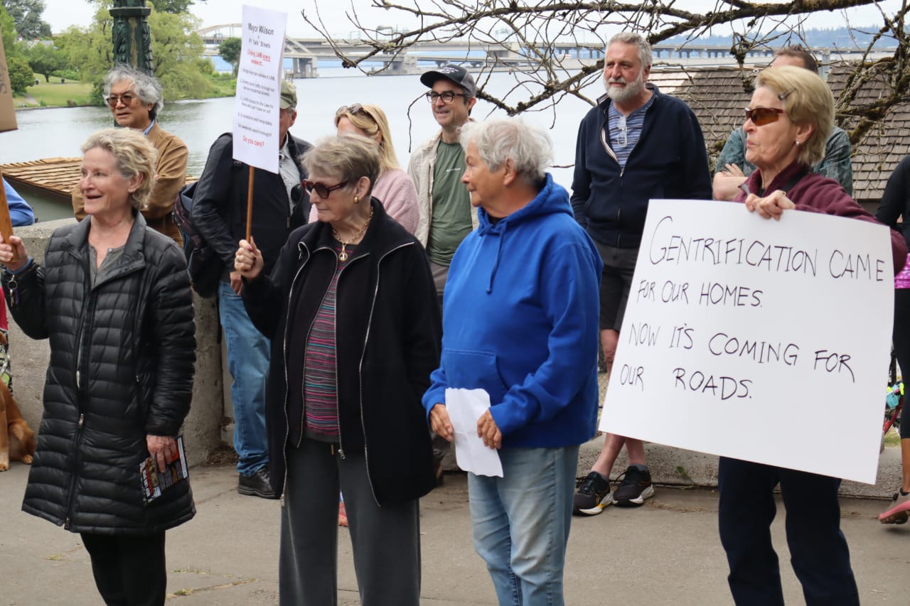 Un grupo de personas, en su mayoría ancianos, portan carteles de protesta. uno lee 