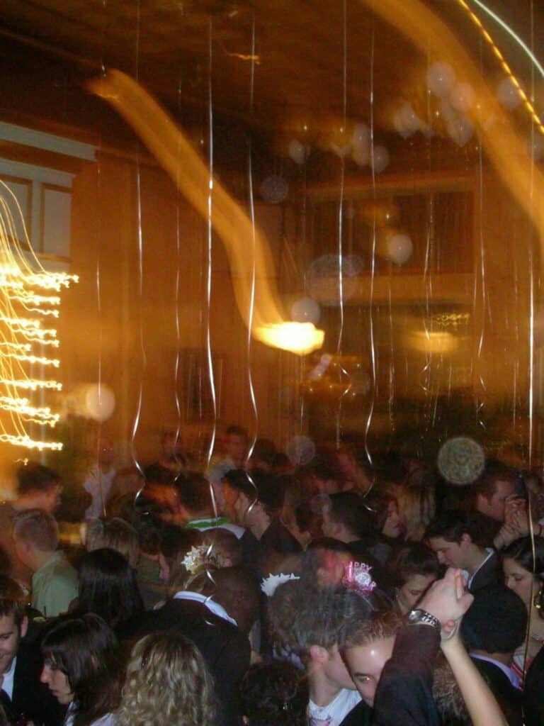 Una fiesta interior llena de gente bailando; Los rayos de luz y el movimiento borroso indican movimiento y poca luz.